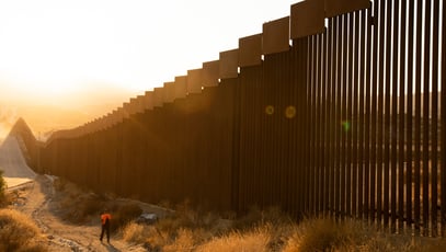 Tecate, Baja California, Mexico - September 14, 2021: Late afternoon sun shines on the USA Mexico border wall people walk in front of it.